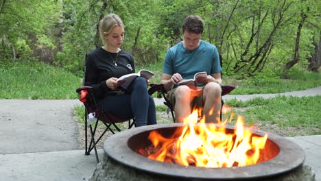 Zwei-Erwachsene-Lesen-Bücher-Am-Lagerfeuer,-Statische-Außenaufnahme