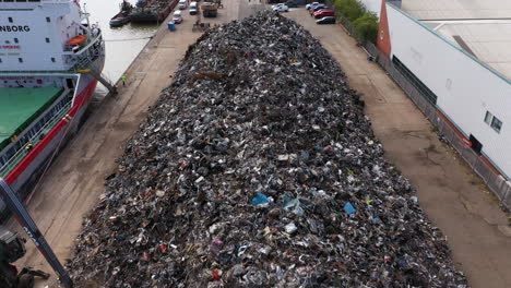 Aerial-reveal-of-a-large-mound-of-scrap-metal-being-loaded-onto-a-ship-to-be-sent-for-recycling