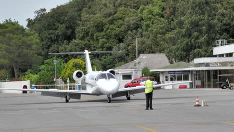 Aircraft-Marshaller-In-Safety-Vest-Signals-The-Pilot-Of-A-Cessna-Citation-Jet-At-The-Airport-With-Marshalling-Wands