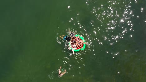 Aéreo,-Grupo-De-Amigos-Jugando,-Empujándose-Unos-A-Otros-Desde-Una-Balsa-Al-Lago