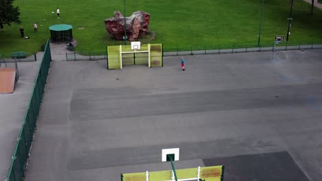 Vista-Aérea-Del-Ejercicio-De-Baloncesto-De-Tiempo-Libre-Masculino-En-El-Patio-De-Juegos-De-Un-Parque-Público-Suburbano-A-La-Izquierda-En-órbita