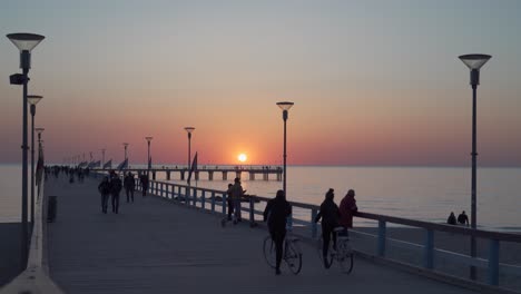 Gente-Caminando-En-El-Muelle-De-Palanga-A-última-Hora-De-La-Tarde-Con-Puesta-De-Sol-En-El-Cielo-Y-Banderas-Ondeando-En-El-Viento