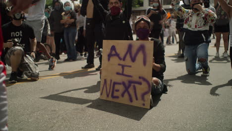 Women-holding-a-sign-during-the-day-at-a-protest-surrounded-by-protestors-and-police