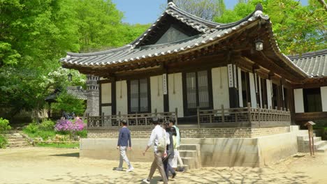 Turistas-Con-Mascarilla-Caminando-En-Un-Día-Soleado-Pasando-Por-Casas-Tradicionales-En-El-Pueblo-Folclórico-Coreano-En-La-Ciudad-De-Yongin,-Seúl,-Corea-Del-Sur