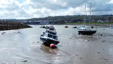 Aerial-view-moored-boats-on-Welsh-low-tide-seaside-breakwater-harbour-coastline-low-angle-forward-shot