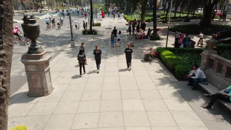 Aerial-low-angle-above-people-walking-at-sidewalk,-cyclists-in-background