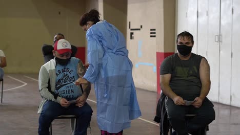 Medium-close-shot-of-a-nurse-applying-a-shot-of-COVD-19-vaccine-to-a-tattoed-latino-man-inside-a-makeshift-vaccination-center