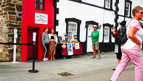 Guía-Turística-Tradicional-Galesa-Fotografiando-Turistas-Fuera-De-La-Famosa-Casa-Roja-Pequeña-Atracción-De-Gales-Conwy