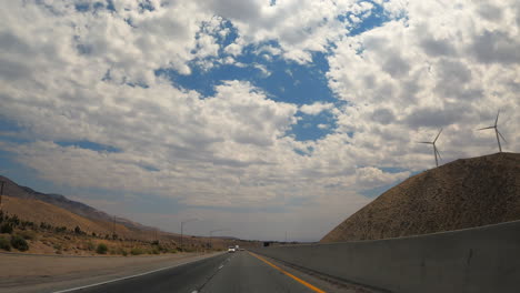 A-scenic-view-from-the-out-the-back-car-window-while-driving-down-the-highway-with-wind-turbines-on-the-hill---slow-motion