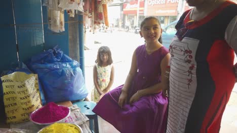 Triste-Y-Pobre-Niña-Asiática-De-Piel-Oscura-Mirando-A-Una-Niña-Rica-Comprando-Polvo-De-Color-Para-El-Festival-Holi-De-La-Tienda