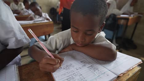 Sad-African-black-boy-writing-and-studying-at-school-with-children-in-the-background-class