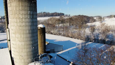 Antena-Descendiendo-Sobre-Tierras-De-Cultivo-Cubiertas-De-Nieve-Con-Silos,-Nevando