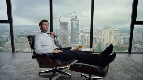 Businessman-sitting-on-chair-in-modern-interior.-Professional-adjusting-tie
