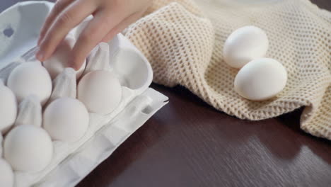 Chicken-eggs-in-carton-on-kitchen-table.-Hand-takes-out-eggs-from-carton