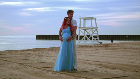 Pregnant-couple-on-sea-beach-at-sunrise.-Love-couple-hugging-on-beach-sea