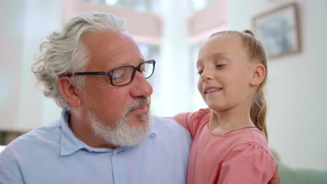 Smiling-grandfather-looking-at-granddaughter.-Girl-hugging-senior-man-in-room