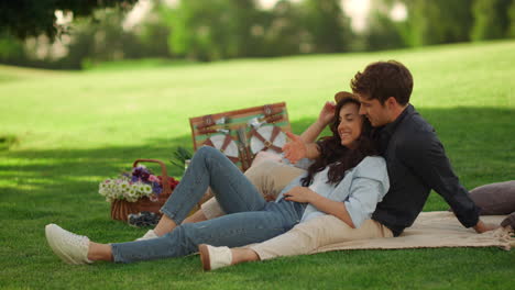 Young-man-and-woman-laughing-outdoors.-Girl-and-guy-sitting-on-blanket-in-park