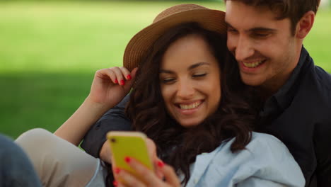 Sweet-girl-and-guy-scrolling-phone-in-park.-Guy-pointing-on-screen-outdoors