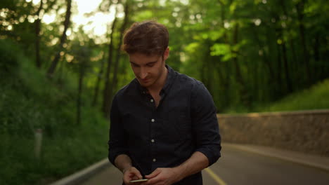 handsome-man-taking-phone-out-of-pocket-outdoors.-Guy-texting-message-in-park