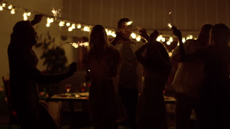 Friends-dancing-on-backyard.-Happy-guys-and-girls-holding-sparklers-in-hands