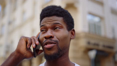 Cheerful-afro-guy-having-phone-conversation-on-street.-Man-talking-in-city