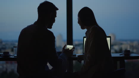 Silhouette-of-relaxed-couple-watching-video-on-mobile-phone-in-office.