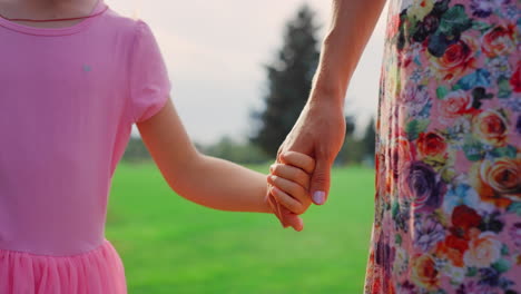 Unknown-woman-and-girl-walking-in-city-park.-Mother-and-daughter-holding-hands.