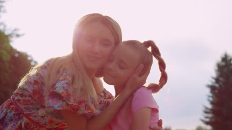 Happy-family-spending-time-outdoor.-Woman-hugging-girl-in-city-park-at-sunset.