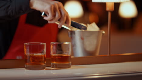 Barman-hands-preparing-whiskey-for-people-in-nightclub.-Man-putting-ice-cubes