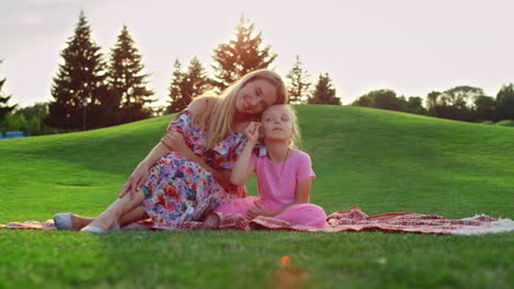 Family-posing-at-sunset-time-at-meadow.-Woman-hugging-girl-in-city-park.