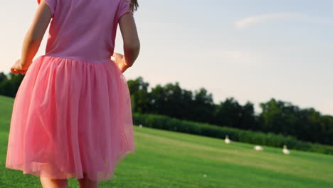 Unrecognizable-girl-in-pink-dress-walking-barefoot-in-sunrise-city-park.