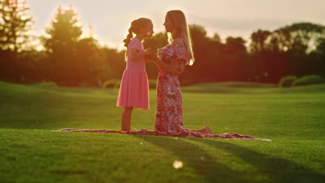 Mother-hugging-daughter-in-city-park.-Woman-talking-to-girl-at-meadow-at-sunrise