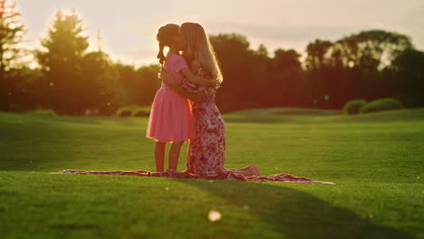 Woman-and-girl-enjoying-sunrise-in-garden.-Mother-hugging-daughter-in-city-park.