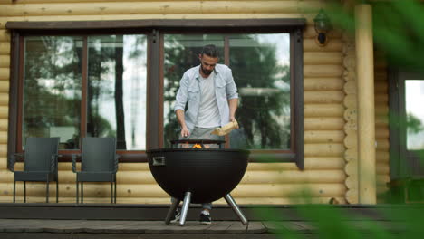 Thoughtful-man-putting-firewood-in-bbq-grill.-Focused-guy-making-fire-in-grill