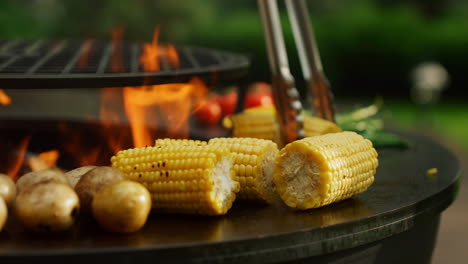 Grilling-vegetables-cooking-on-fire-outside.-Man-hands-turning-corn-with-forceps