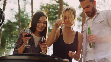 Cheerful-friends-cooking-for-grill-party-outside.-Woman-pouring-salt-outdoors