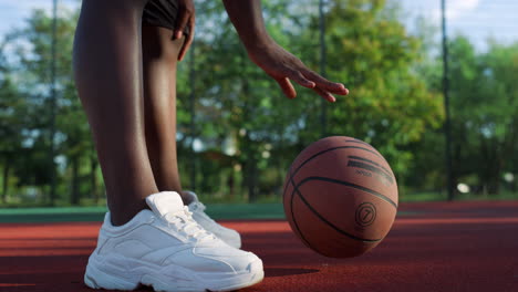 Unrecognizable-african-basketball-player-bouncing-basketball-ball-outdoor.