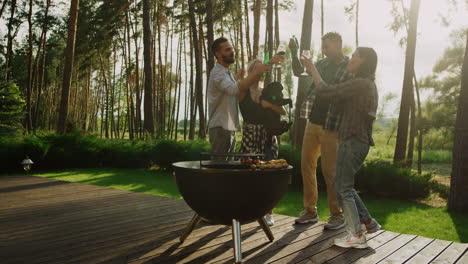 Happy-people-celebrating-on-grill-party-outside.-Playful-guys-clinking-glasses