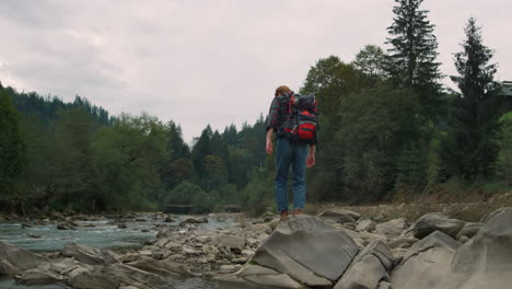 Man-walking-on-rocks-at-river.-Male-tourist-hiking-along-river-in-forest