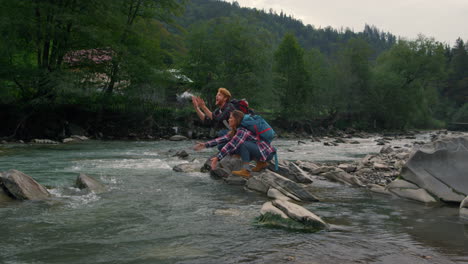 Man-and-woman-sitting-on-rock-at-river.-Couple-splashing-water-in-air