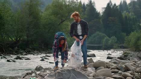 Volunteers-picking-plastic-bottles-on-river-shore.-Couple-collecting-garbage