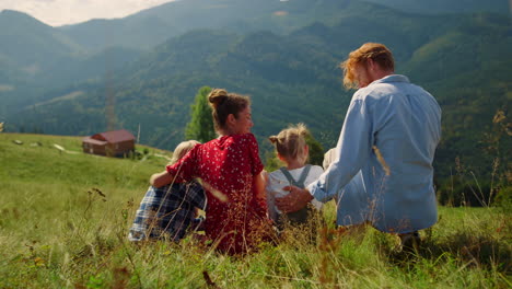 Parents-sitting-grass-mountains-hill-with-children.-Family-hugging-on-meadow.