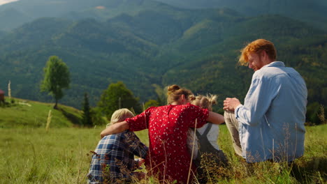 Family-sitting-green-hill-in-front-mountain-panorama.-Mother-hugging-children.