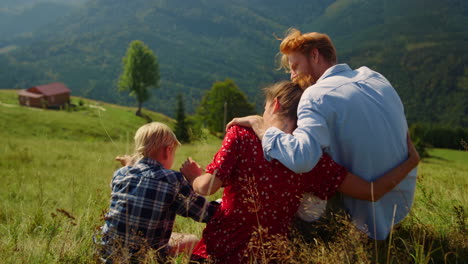 Loving-parents-hugging-sitting-with-son-on-mountain-hill.-Family-enjoying-nature