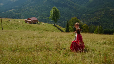 Young-mother-sitting-daughter-on-meadow.-Woman-relaxing-with-girl-in-mountains.