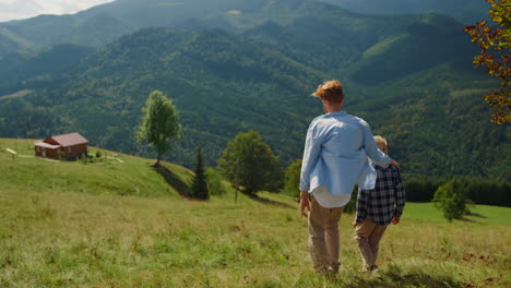 Father-hugging-son-walking-on-mountain-hill.-Man-going-down-green-slope-with-boy