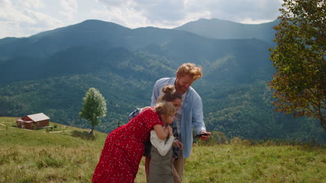 Friendly-family-using-smartphone-in-mountains.-Couple-with-kids-looking-to-phone
