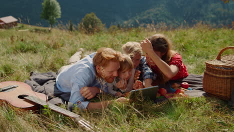 Family-using-tablet-picnic-in-mountains-hill.-Parents-with-kids-looking-screen.