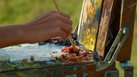 Unknown-artist-mixing-paints-on-palette.-Closeup-hand-drawing-on-canvas-outdoors