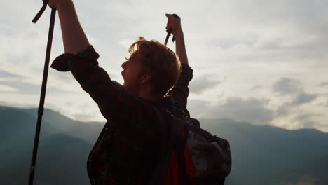 Closeup-euphoric-hiker-celebrate-raise-hands-in-mountains.-Emotional-guy-on-peak